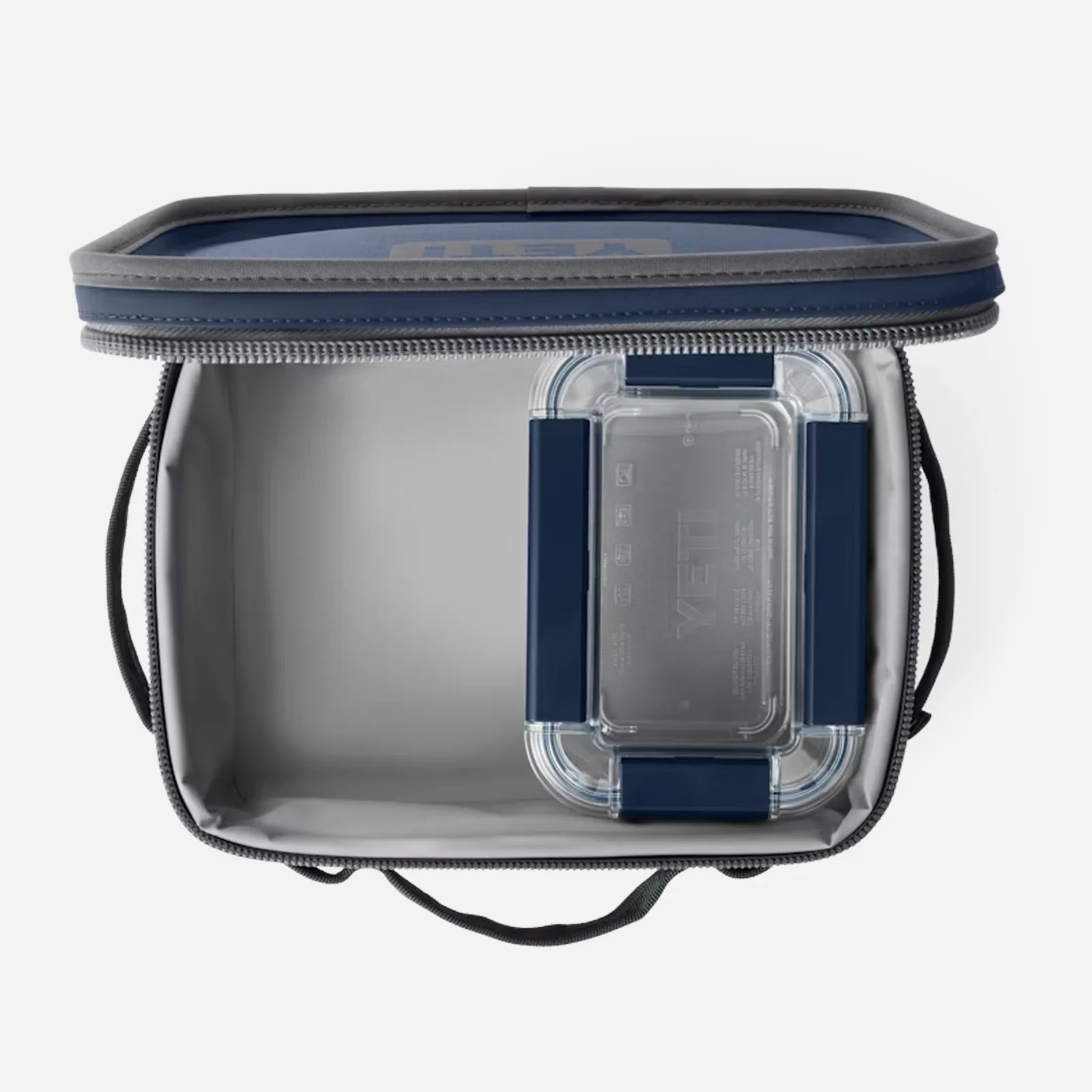 Yeti navy blue hopper cooler shown from above. The lid is open to reveal how a Yeti Food Storage container sits flushly against the right hand edge. Both the cooler and the container are empty. The product is shown against a light grey background. 
