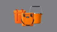 A Yeti cooler backpack, roadie cooler and ice bucket aligned next to each other in bright king crab orange. The product images are sitting against a dark grey background.
