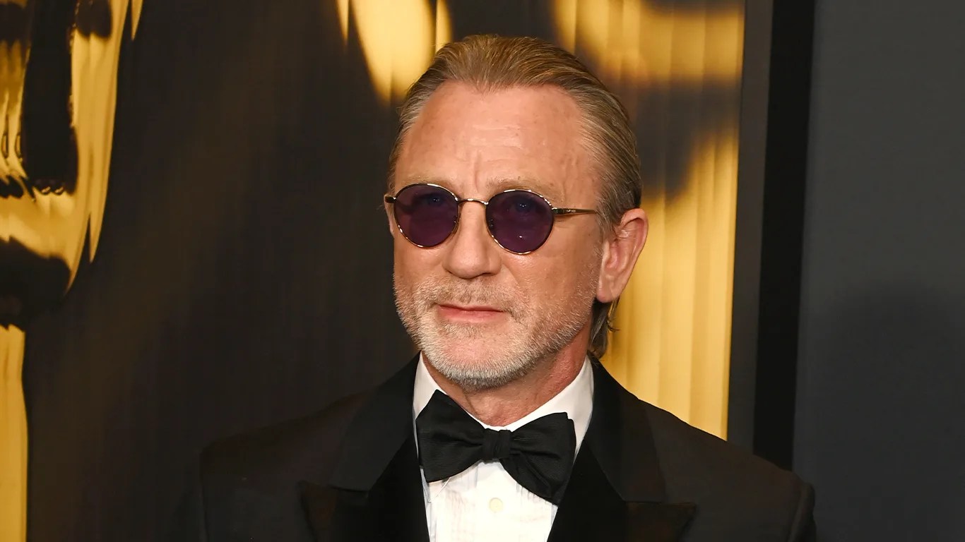 actor daniel craig poses on a red carpet wearing an omega watch out of frame