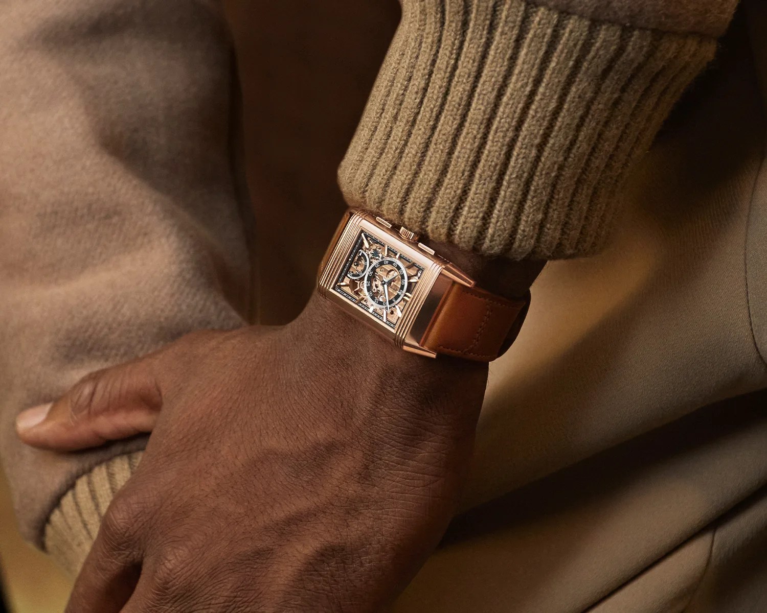a gold jaeger lecoultre reverso dress watch on the wrist of a man wearing a sweater