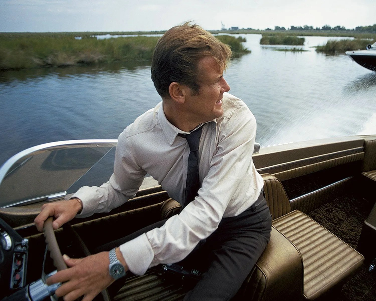 roger moore as james bond wears a tissot watch while driving a boat in the film live and let die