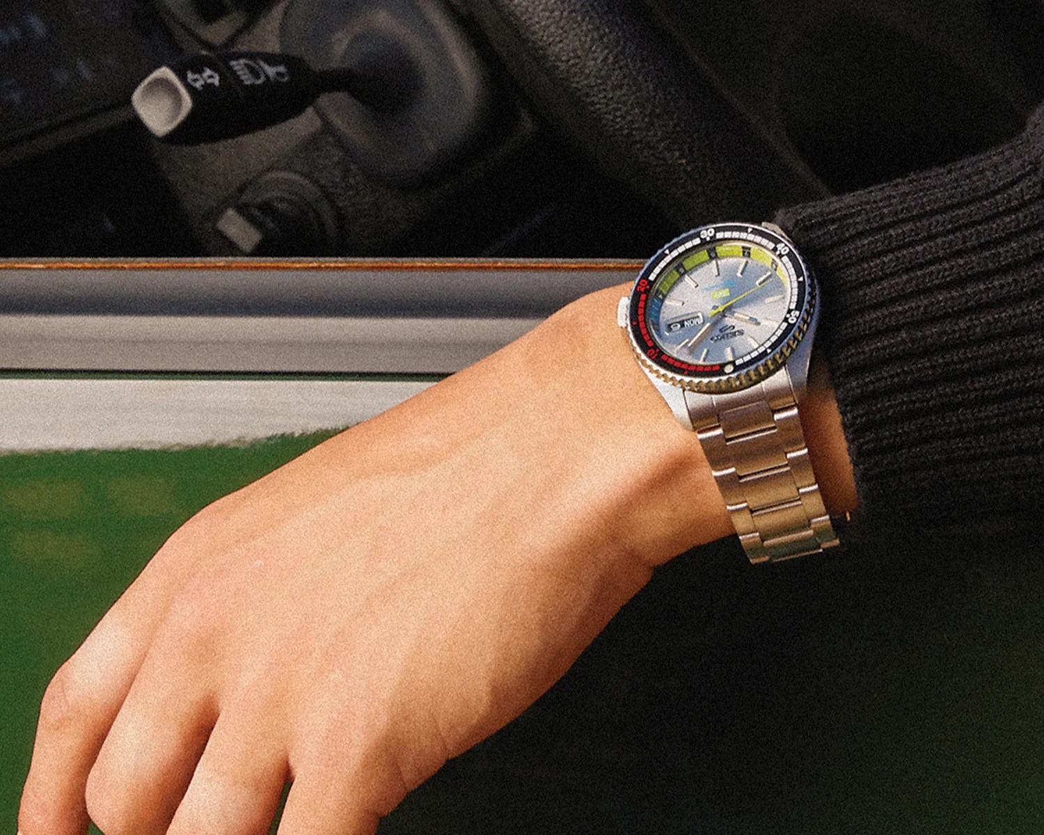 a man puts his hand out a car window while wearing a seiko x huf watch on his wrist
