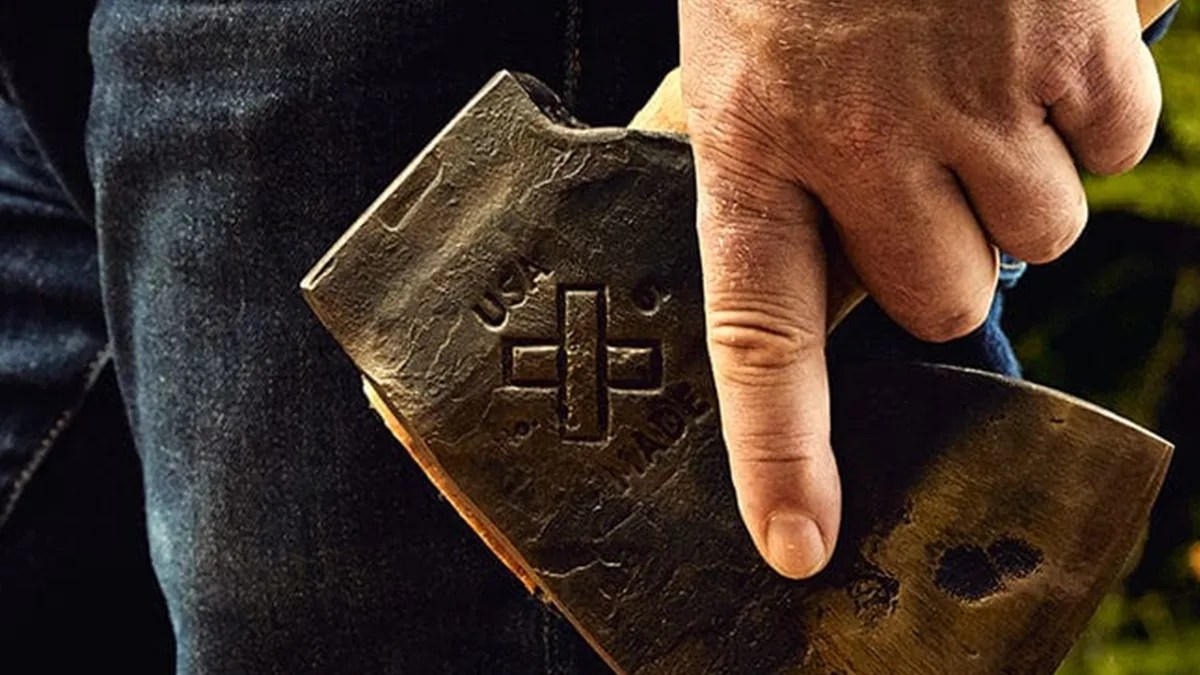 Macro shot of Best Made Co Old Gold No 1 axe in man's hand in front of blue jeans and forest background
