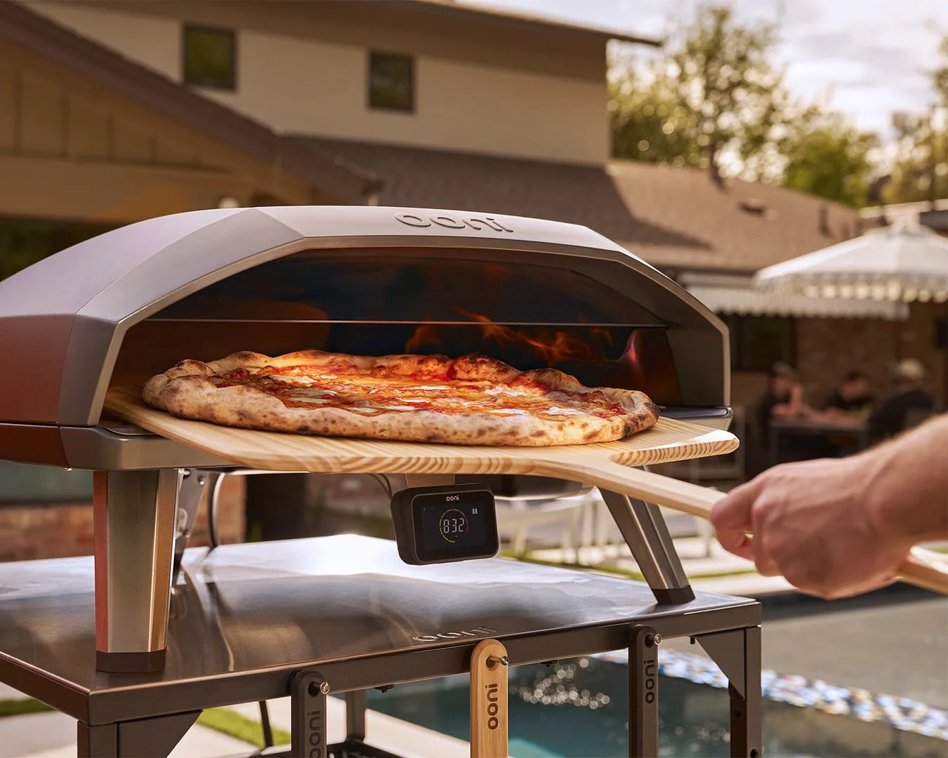 hand using a large paddle to place pizza into Ooni Koda 2 Max Gas Powered Pizza Oven
