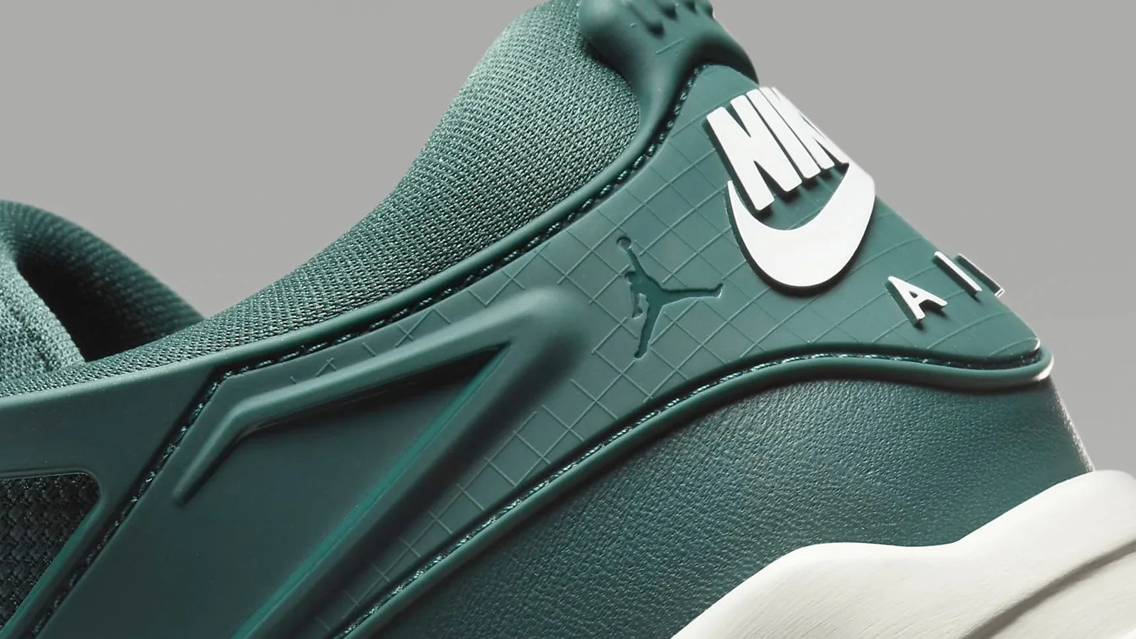A close up crop of the heel of the Air Jordan RM4 sneaker. The sneaker is a dark forrest green with cream color logo and trim
