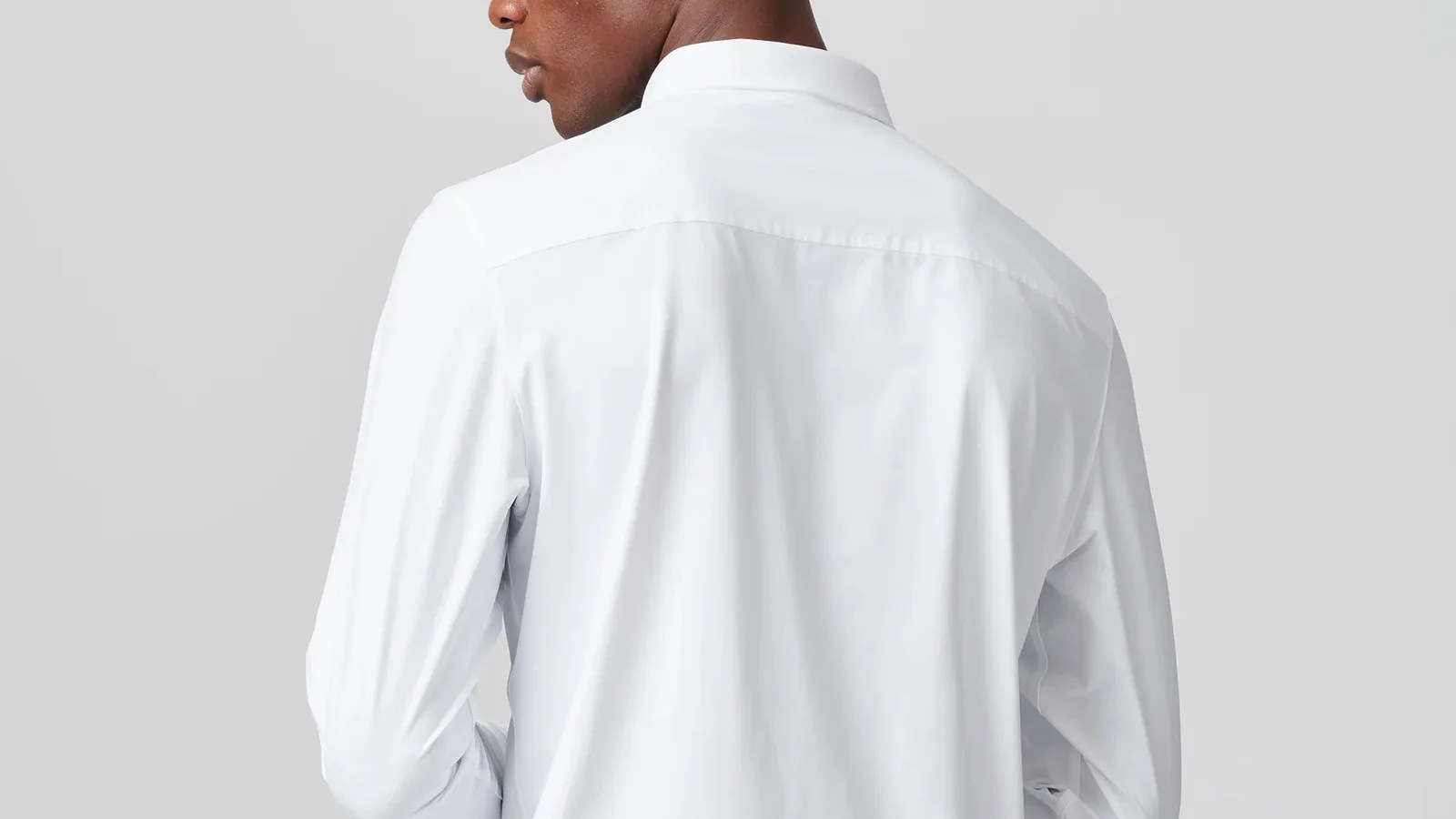 A man wearing a white Rhone commuter dress shirt photographed form behind