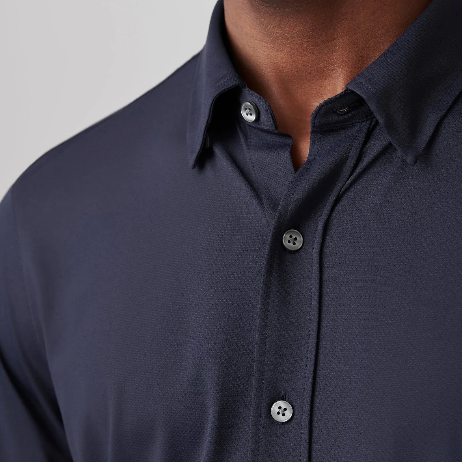 Rhone Commuter dress shirt in dark navy shown up close on a black male model. The image shows the top buttons and collar.