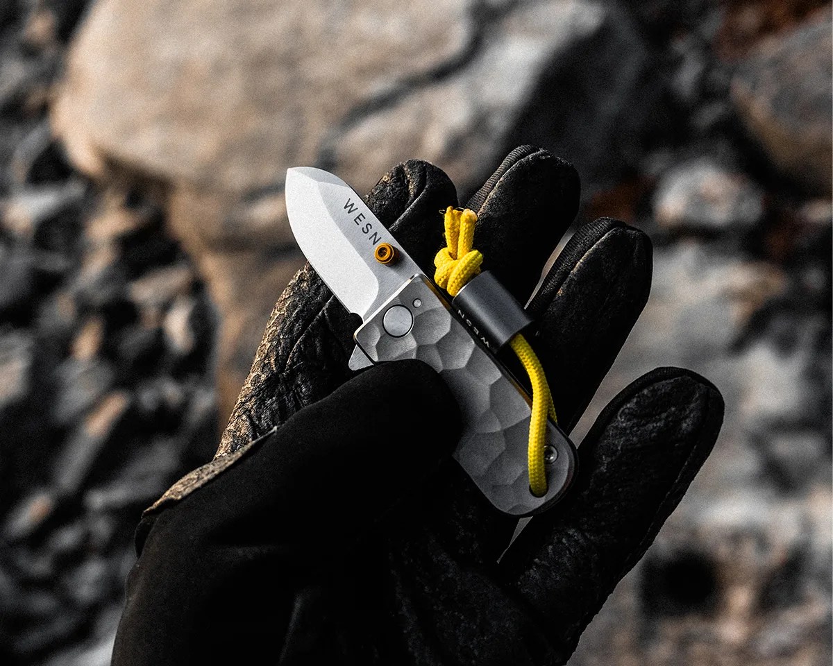WESN Ridgeback Microblade held by gloved hand over rocky landscape