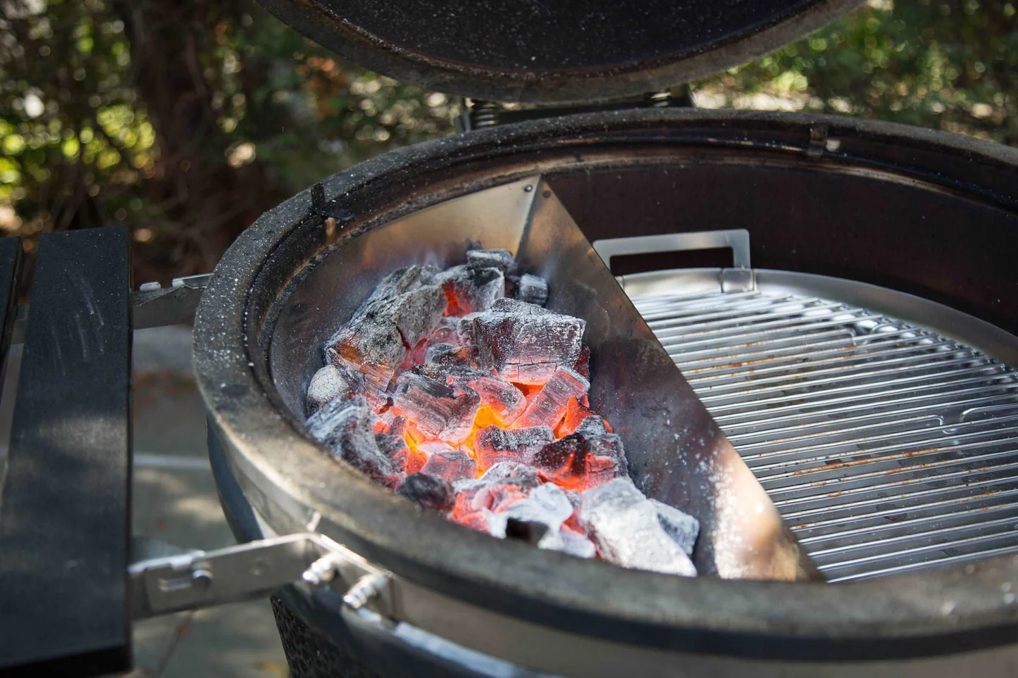 A photo of a Slow N' Sear basket filled with charcoal sitting in a charcoal grill. The coals are hot and burning.