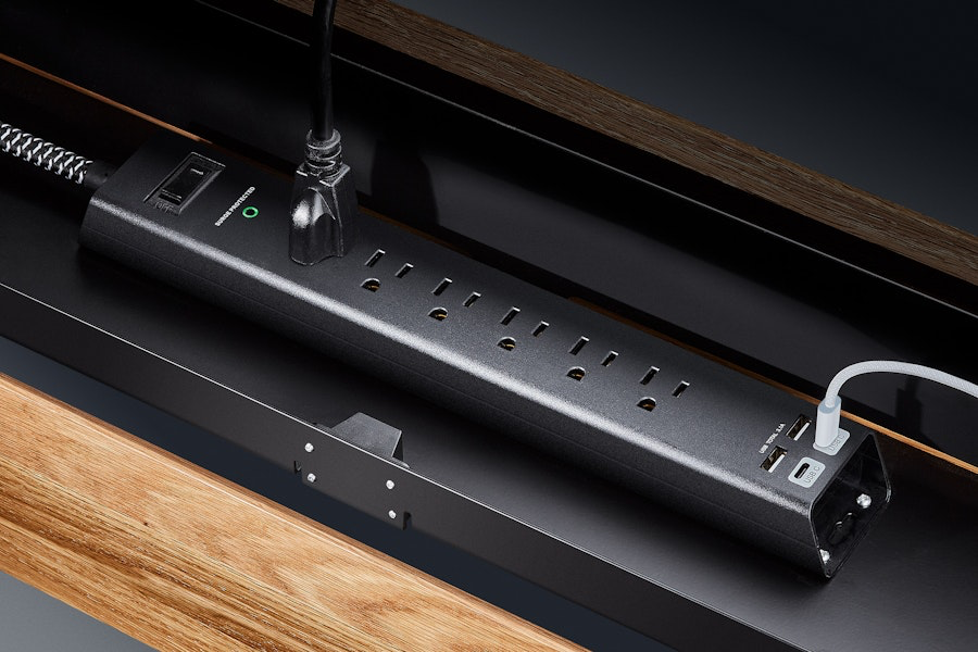 An image showing the Grovemade Desk's integrated surge protector sitting in the hidden metal compartment that hangs underneath the back of the desk surface. 