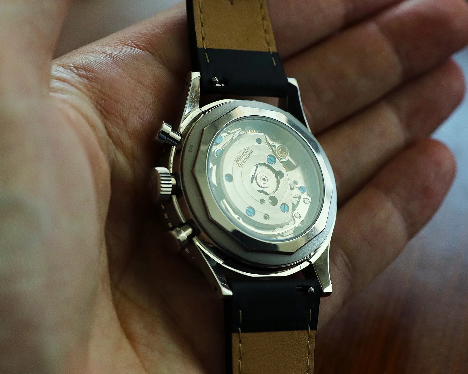 a hand holds a nivada grenchen chronograph watch showing the mechanical movement through its clear caseback