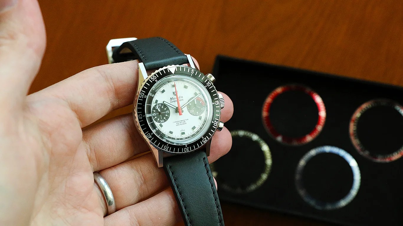 a hand holds a nivada grenchen chronograph watch over some watch bezels