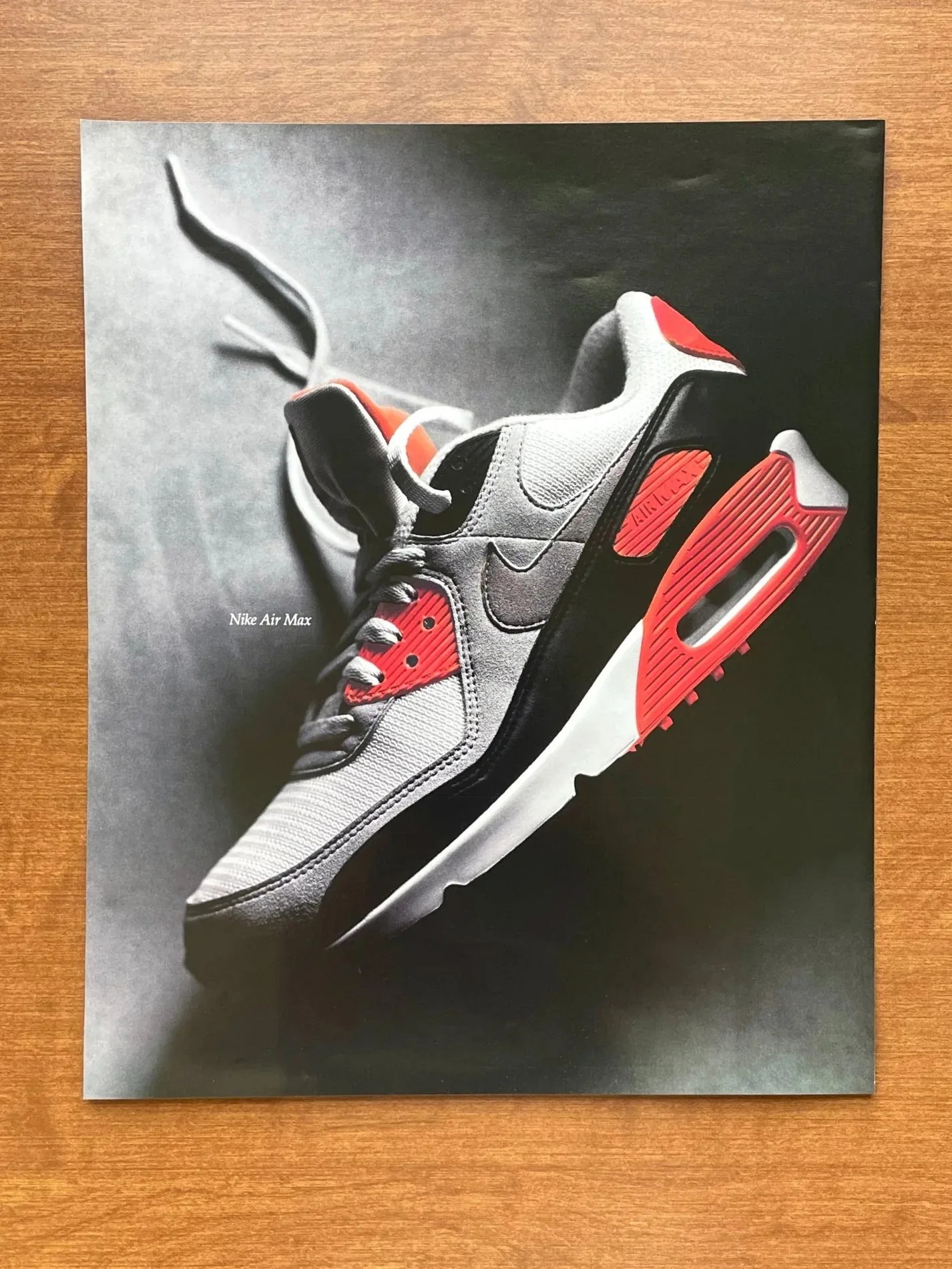 A picture of a vintage Nike Air Max 90 print magazine ad sitting on a wooden table. 