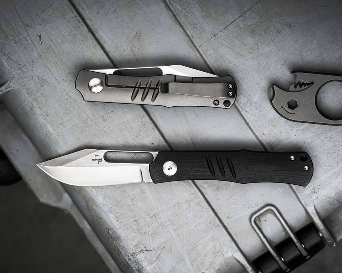 two Böker Sliplock knives, one closed and one opened, sitting on top of a rugged carry case next to a Bomber bottle opener