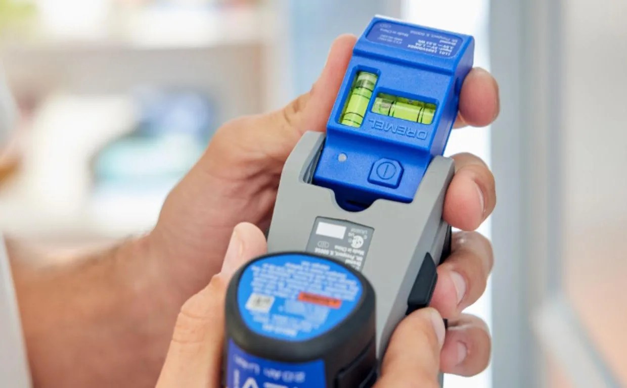 The Dremel Blueprint Multi-Drill shown turned upside down with the devices integrated bubble and laser level being pulled away from its storage compartment the bottom of the drill's front handle.