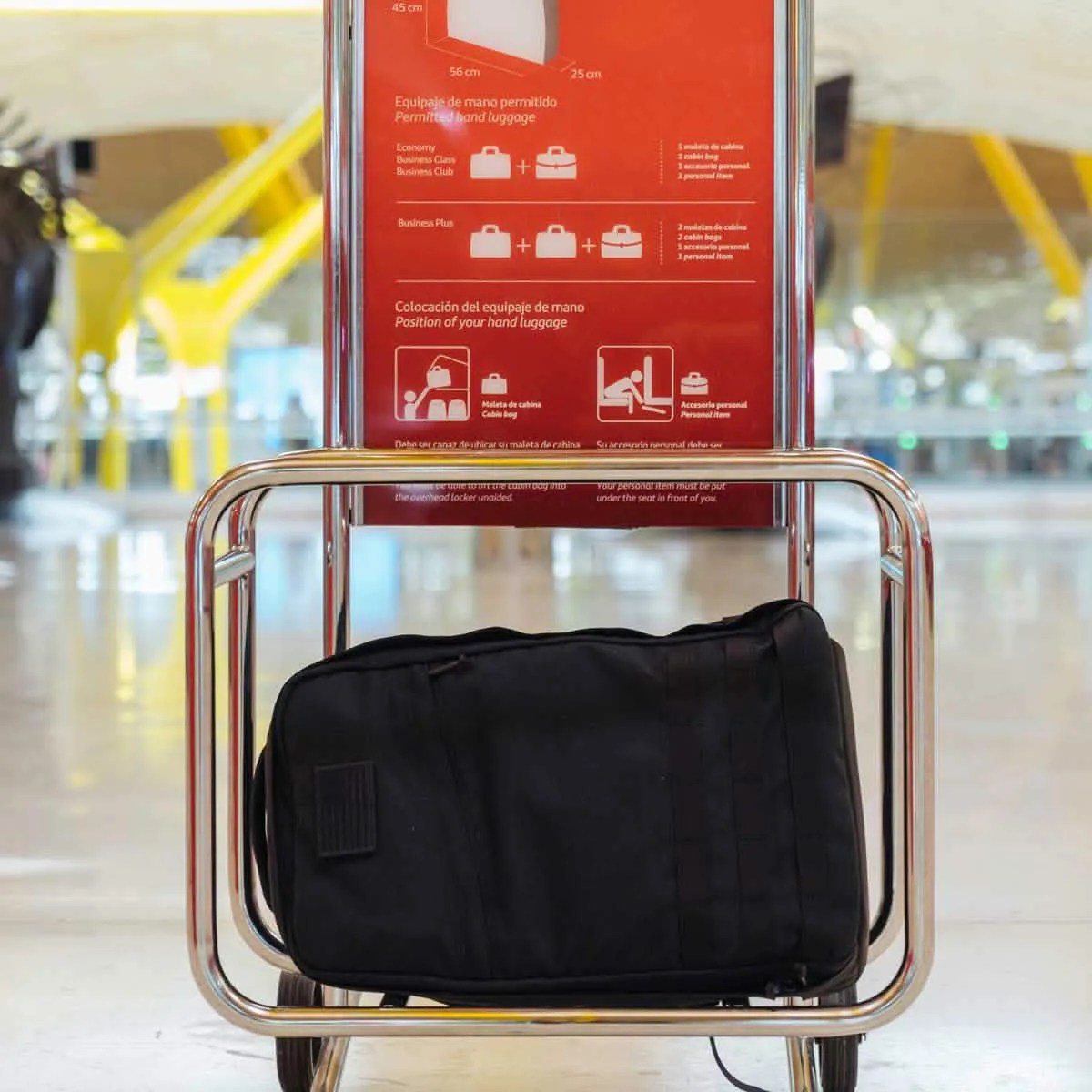 A black GORUCK GR1 is shown resting inside an airline carry-on bag with a metallic frame. The bag is on its side. 