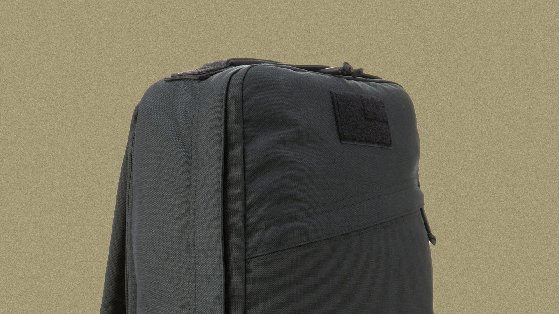 A detailed shot of the upper portion of the GoRuck GR1 in black. The bag is shown against a speckled light tan colored background.