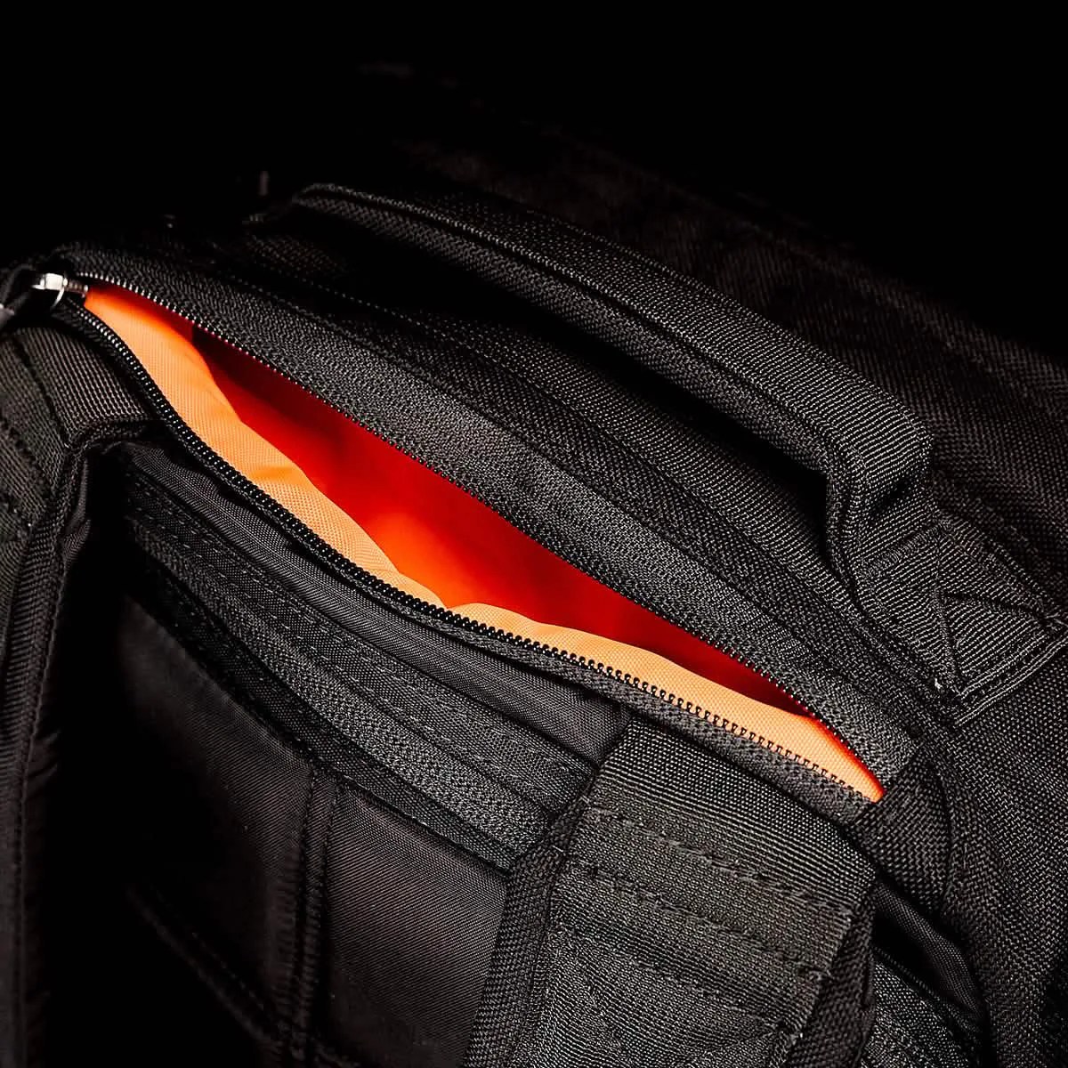 A closeup showing the quick access pocket of the GoRuck GR1 unzipped to reveal a bright orange internal bag lining. 