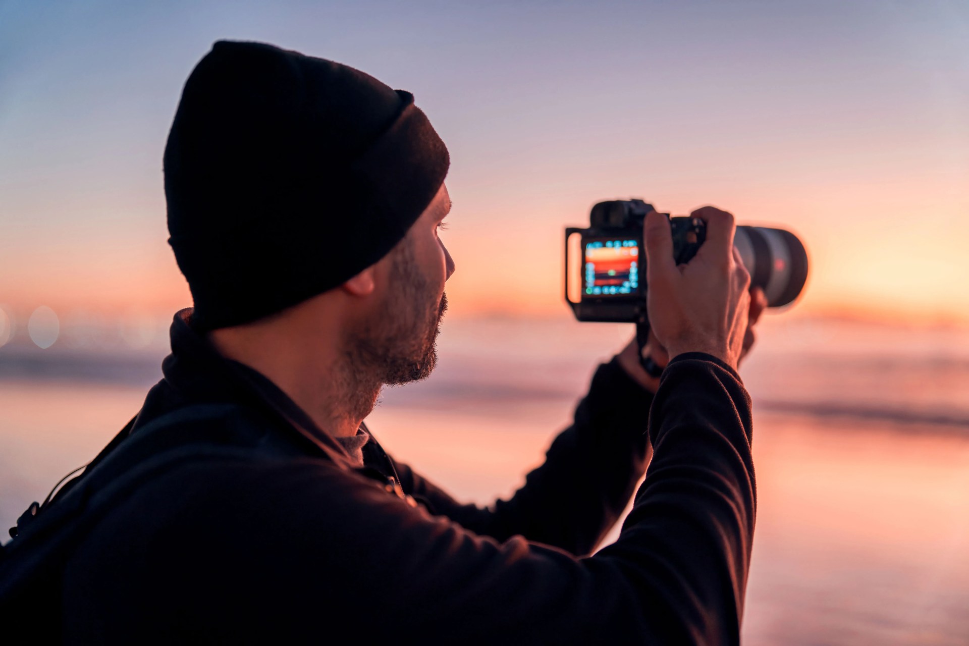man taking picture of a pink sunset with camera