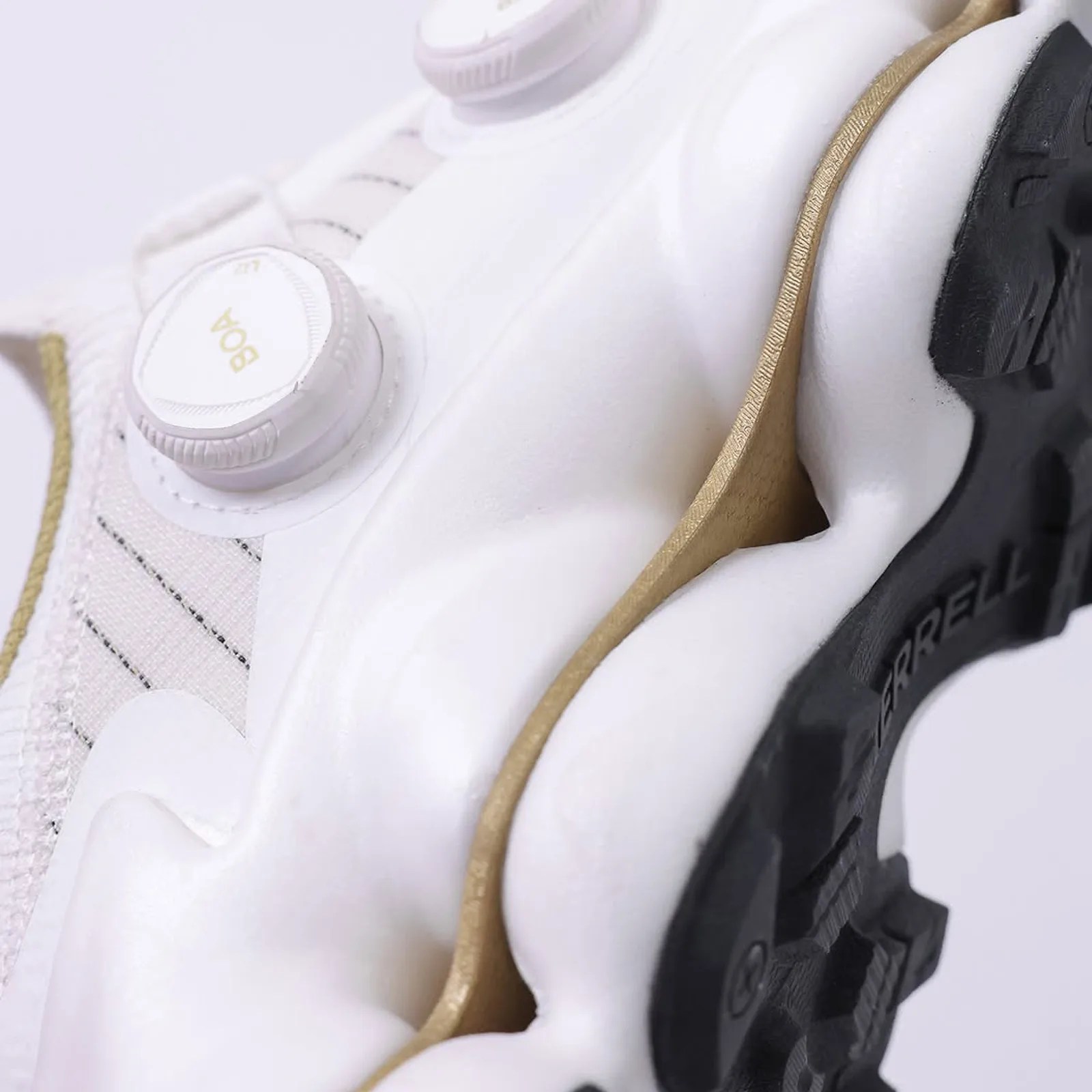 A close up image of the Merrell SpeedARC Surge BOA in white and gold highlighting the shoe's two layers of FloatPro+ SC foam that sandwich the shoe's nylon Flexplate. 