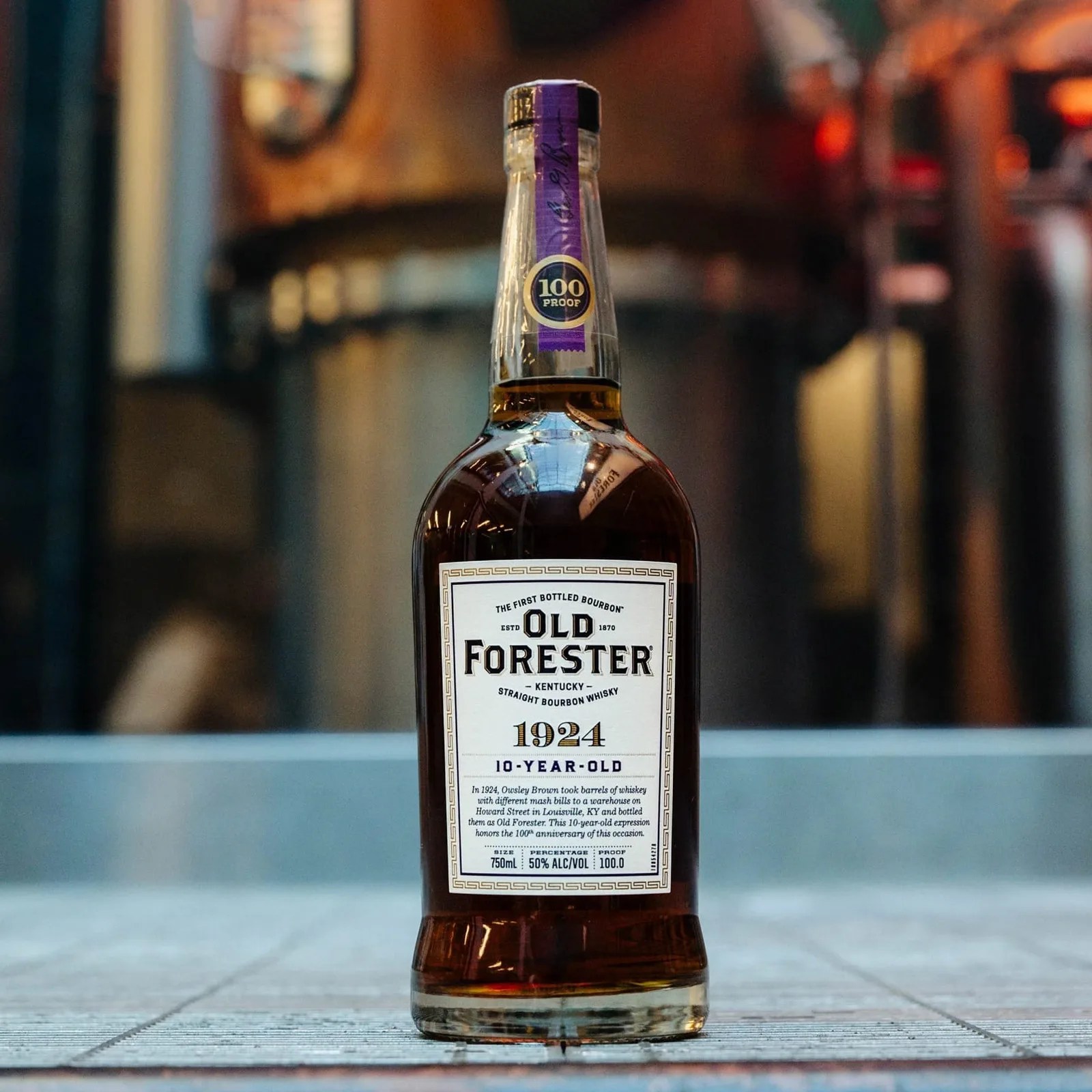 A bottle of Old Forester 1924 shown against a blurred background of a distillery floor