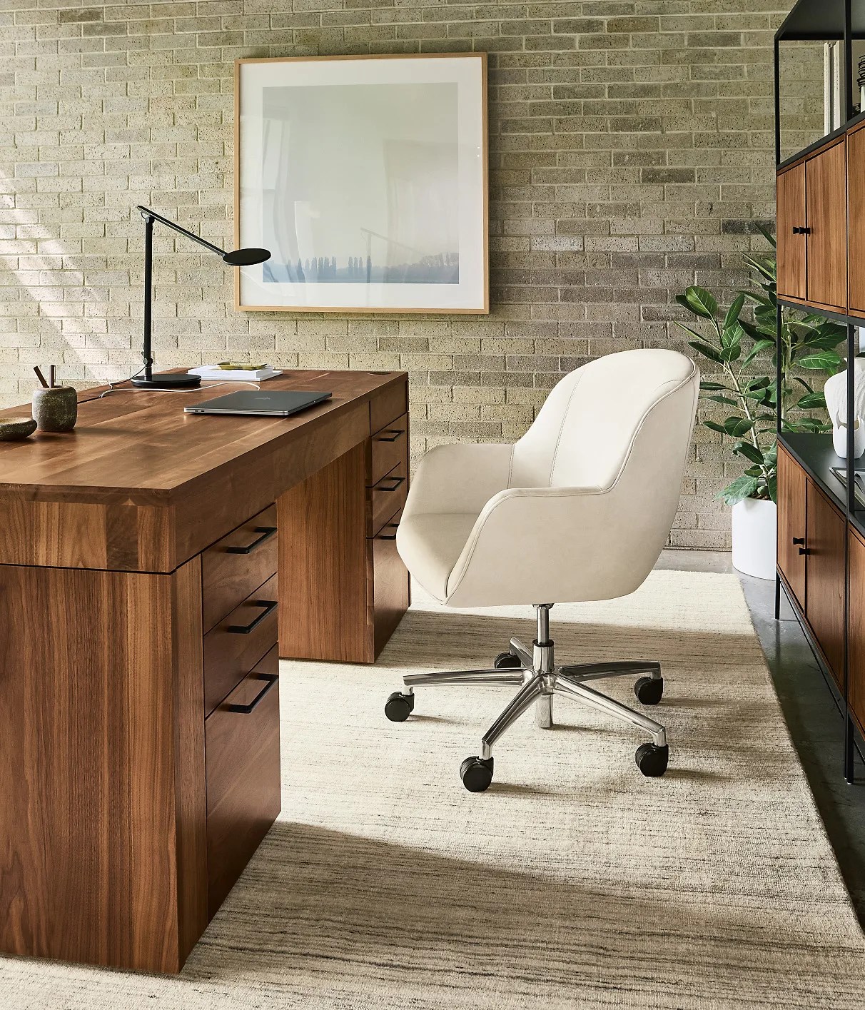 Room&Board Lincoln desk shown in a stylish home office viewed from the side. The desk is in a dark walnut wood with a white fabric desk chairs in front of it. 