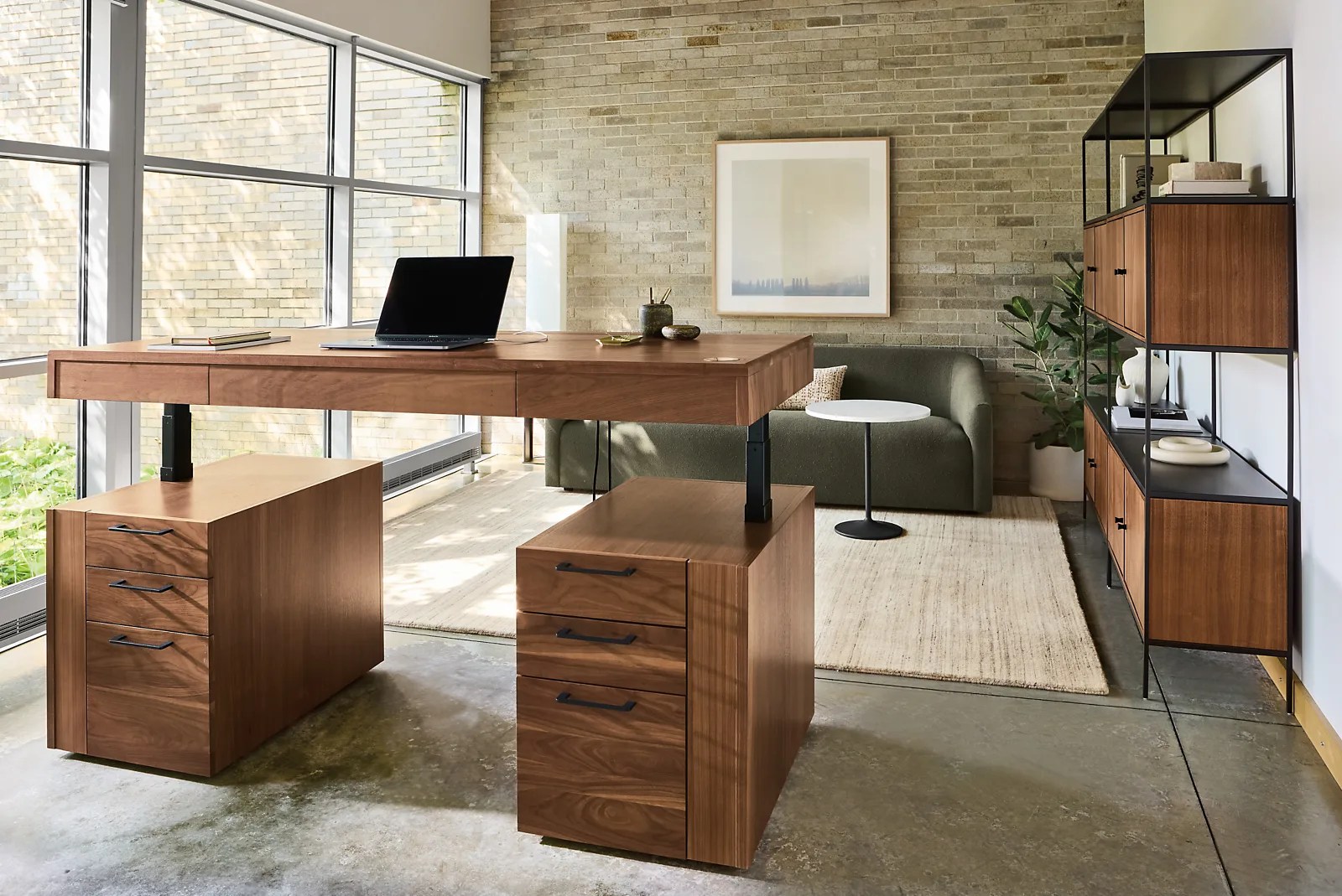 Room&Board's Lincoln Desk in a dark walnut wood shown in a stylish home office. The surface of the desk is partially raised to reveal the desk's standing functionality. A laptop is sitting on the surface.