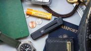 James Brand Chapter knife surrounded by lip balm, coins, keychain, hand sanitizer, Pioneer Carry wallet, passport and notebook on gray background