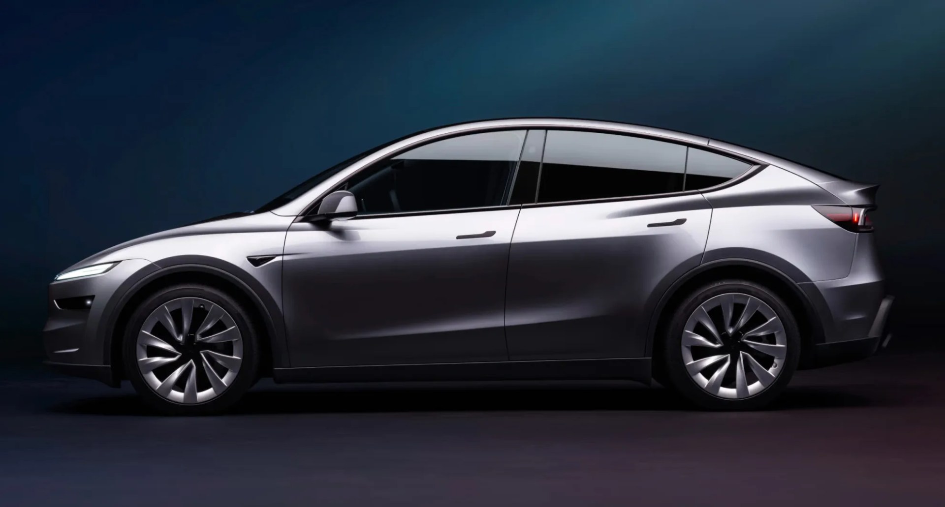 Tesla Model y 2025 edition shown sitting profile on a grey surface against a dark blue background. 