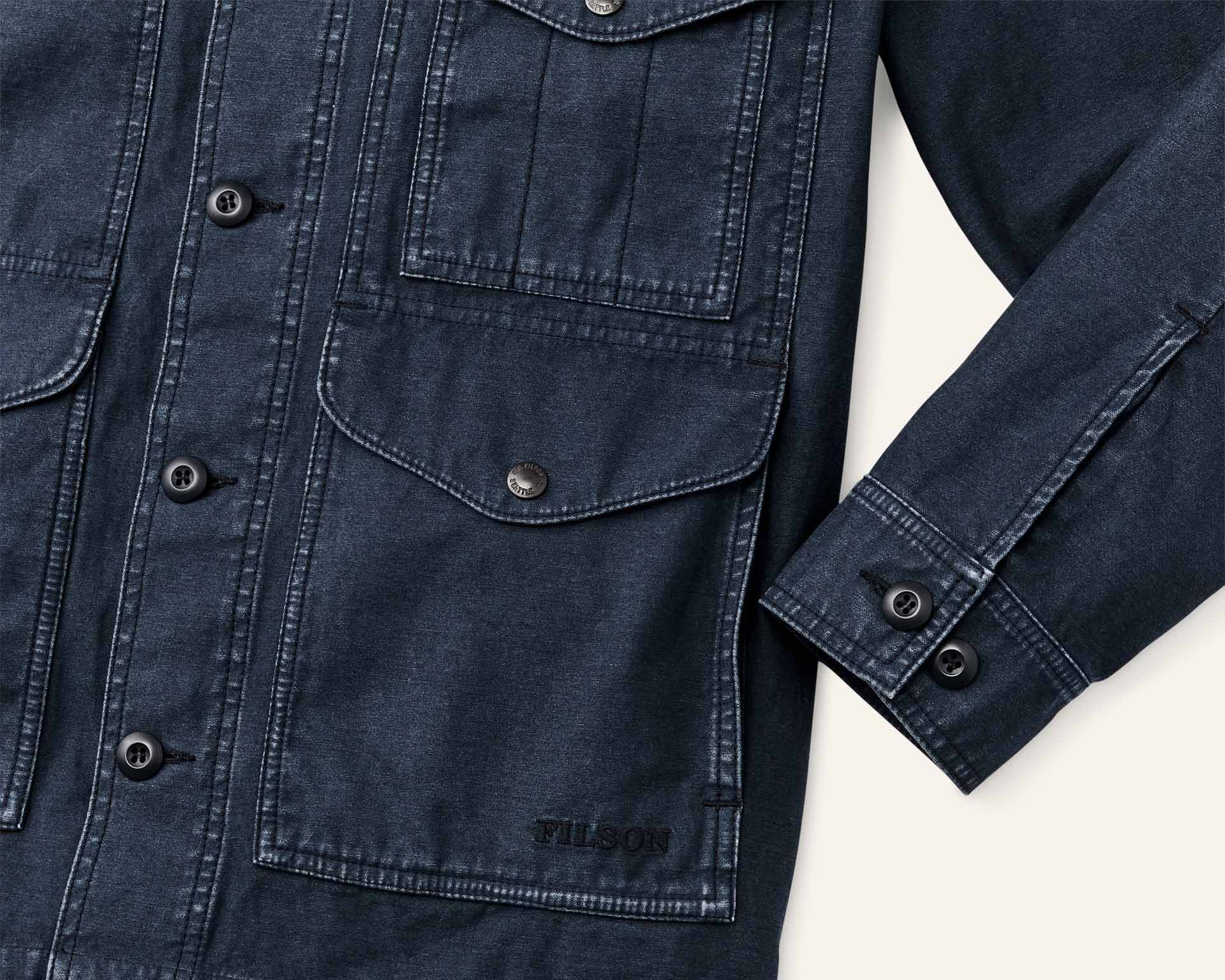 the button cuff and snap flap pocket of a blue canvas jacket