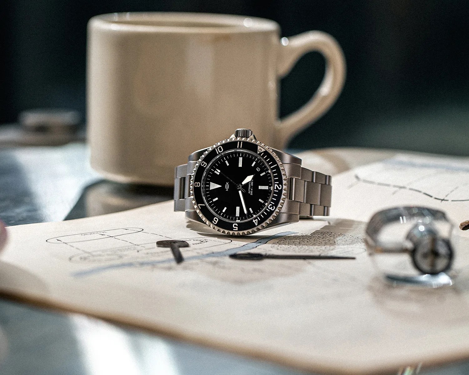 a mk ii dive watch on a table next to a coffee mug