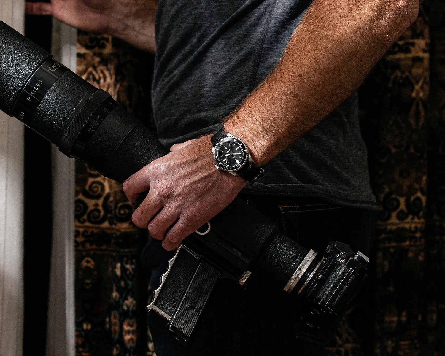 a man wears a Mk II dive watch while carrying a camera with a telephoto lens