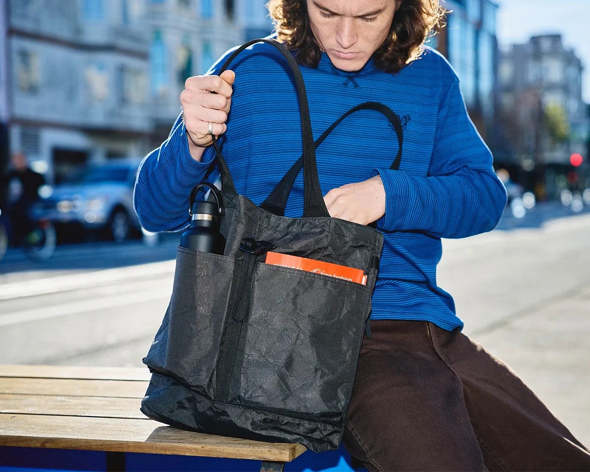 Man inspecting Aer Simple Tote while sitting on city bench