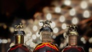 Three tops of different Blanton's Bourbon bottles shown from the neck up against a blurred background of twinkly lights