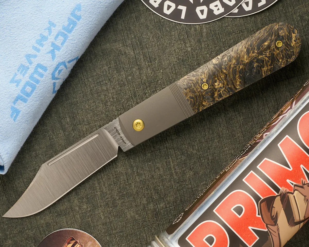 Jack Wolf Knives Primo Jack knife on greenish background next to stickers, towel and aluminum tube