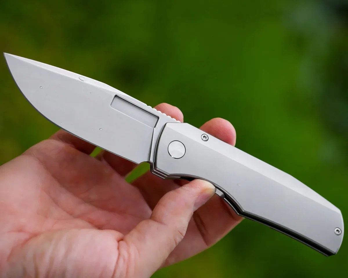 Vero Engineering Nova Mini knife in hand in front of blurry green background