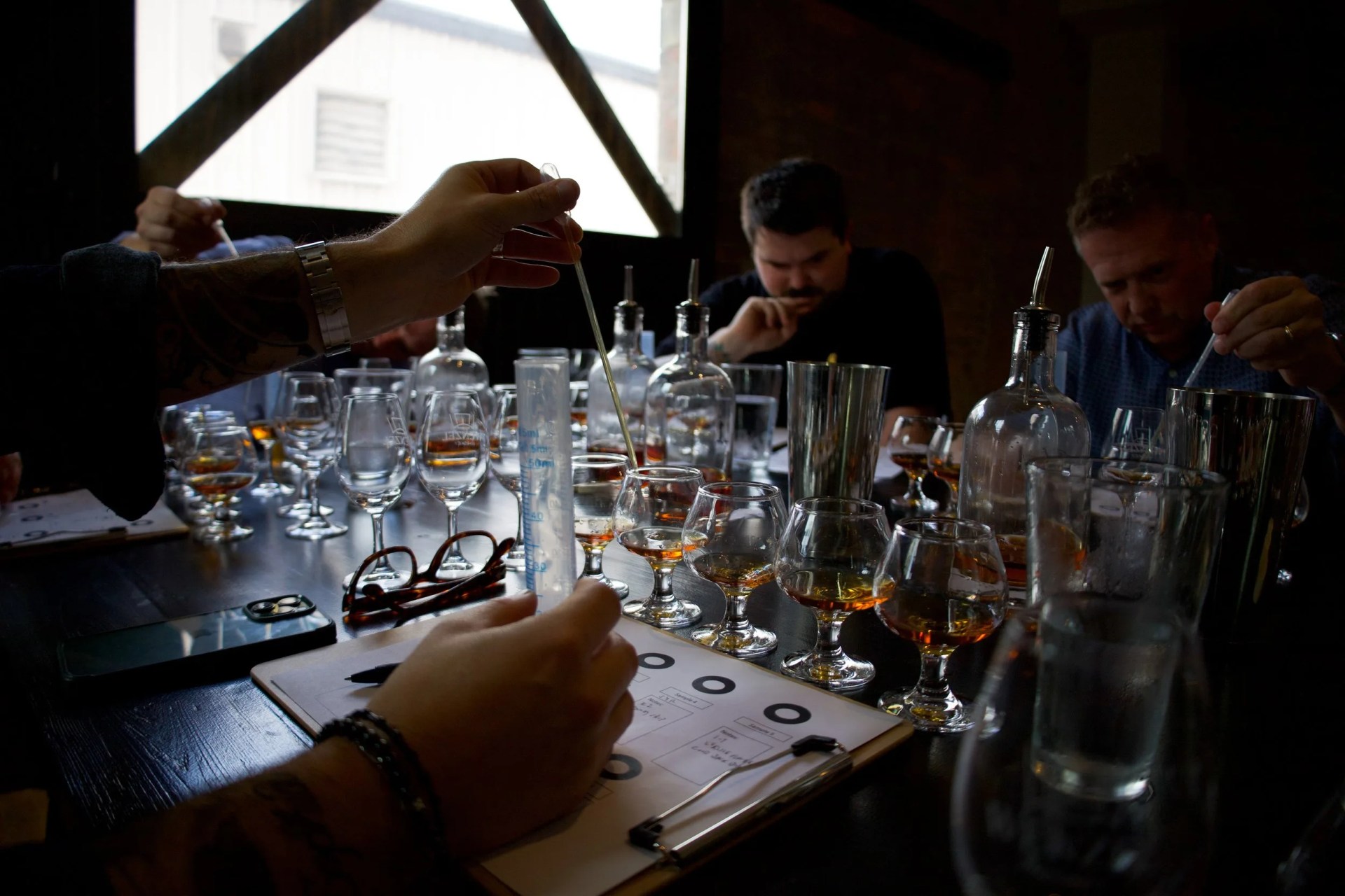 Men sitting around a table filled with whiskey glasses and pipettes blending whiskies together
