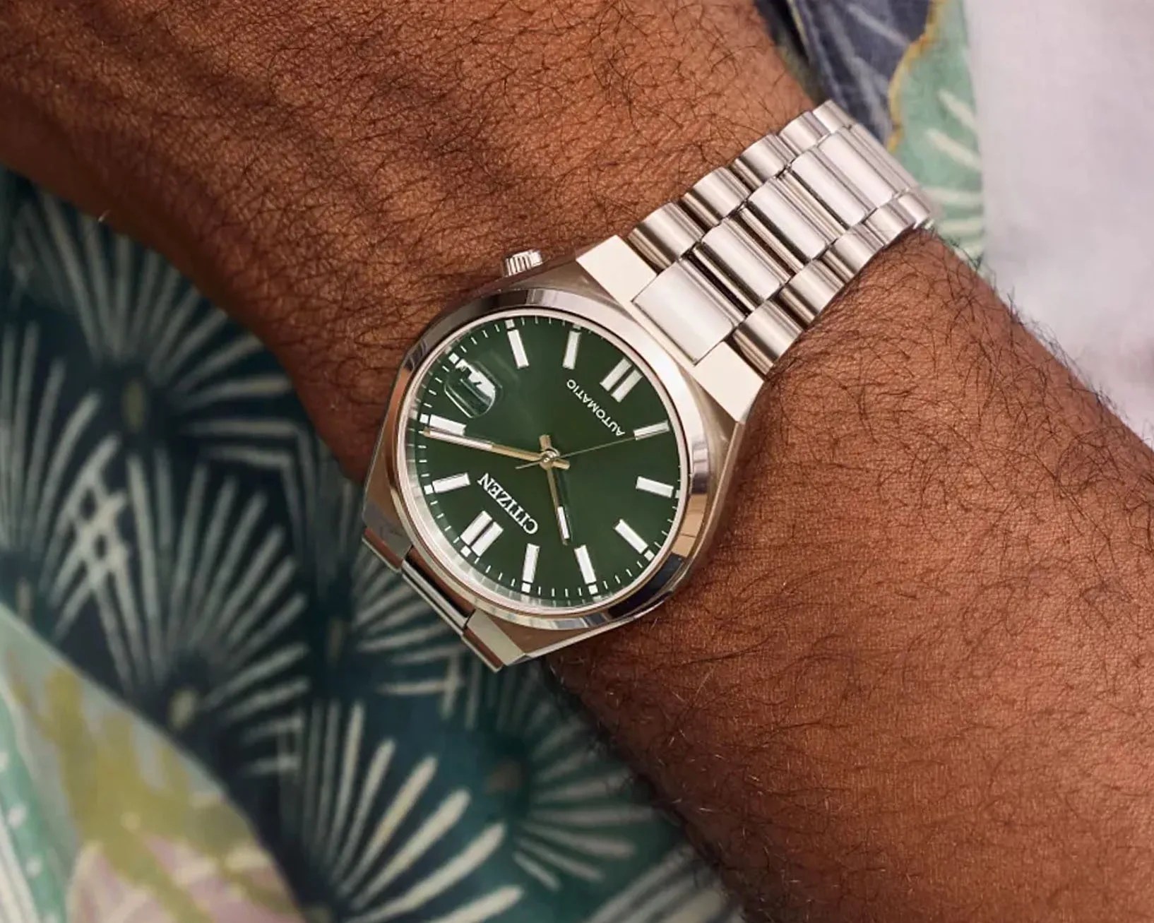 a steel watch with a green face on a man's wrist