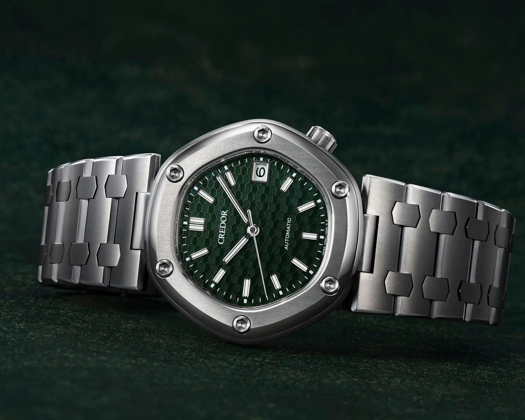 a titanium watch lying on a green fabric