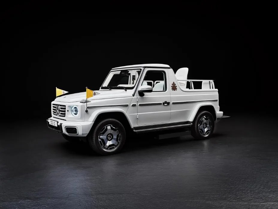 The first electric “Popemobile” from Mercedes-Benz shown parked on a grey surface in an empty black room. The vehicle is a custom electric G-Wagen in white with an open top. 