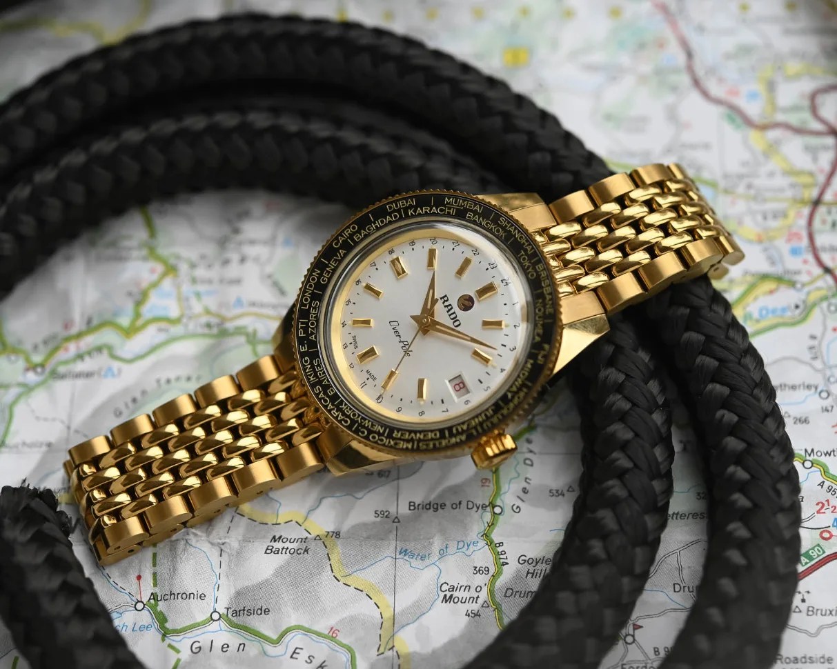 a gold watch with a gold beads of rice bracelet laying on a black rope