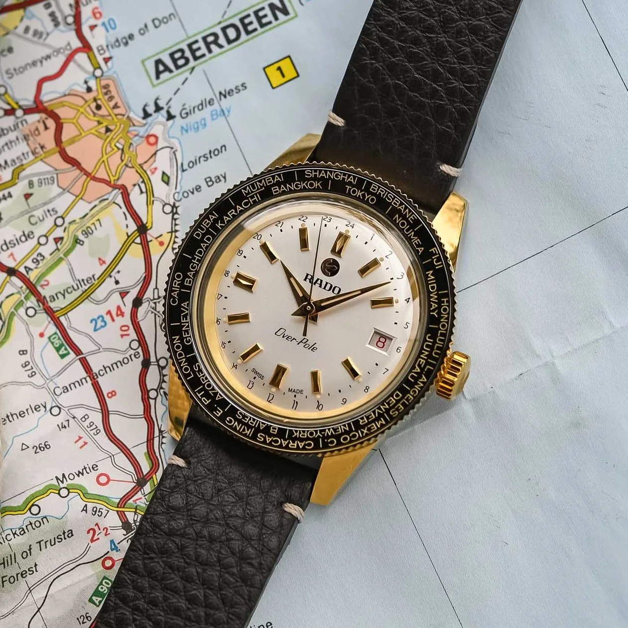 a gold watch with a black leather band laying on a map