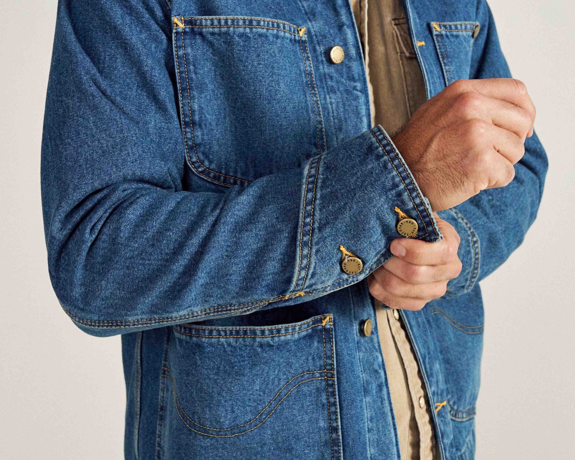 close up of the cuff and pockets of a blue denim chore coat