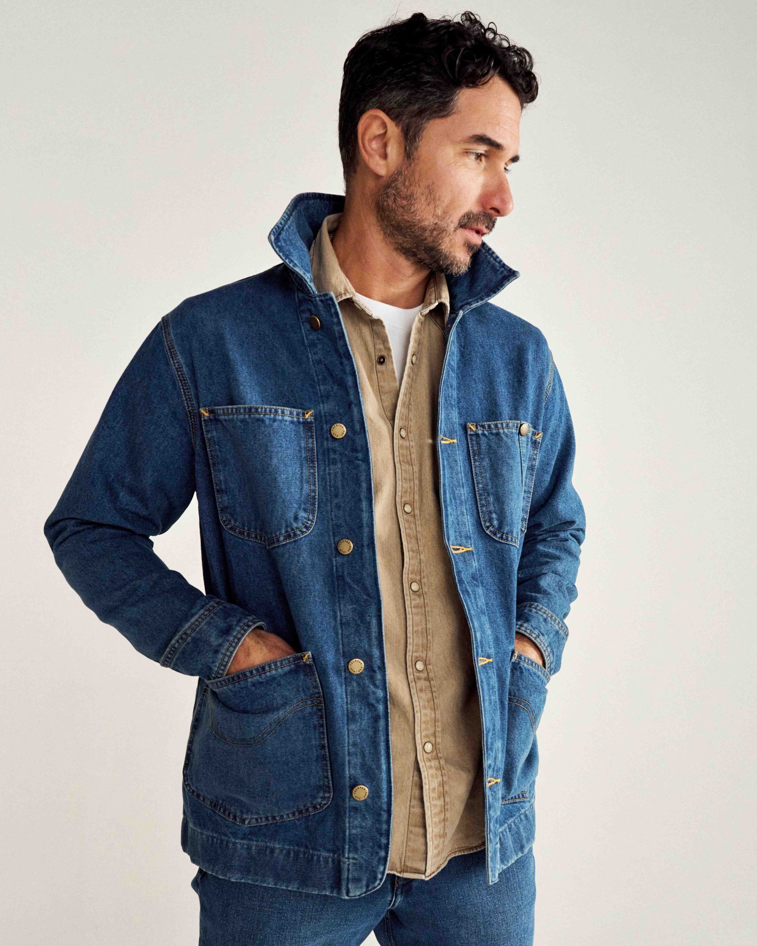 a man in a denim chore coat with his hands in his pockets