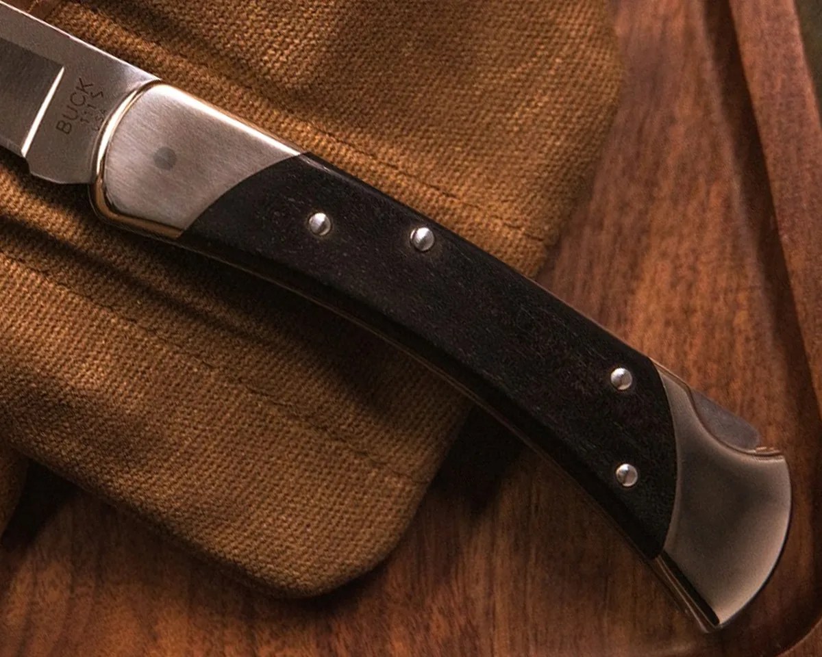 Closeup of Buck 111 Folding Hunter MagnaCut knife handle on nylon EDC pocket above wallet, jacket, valet tray and waxed canvas