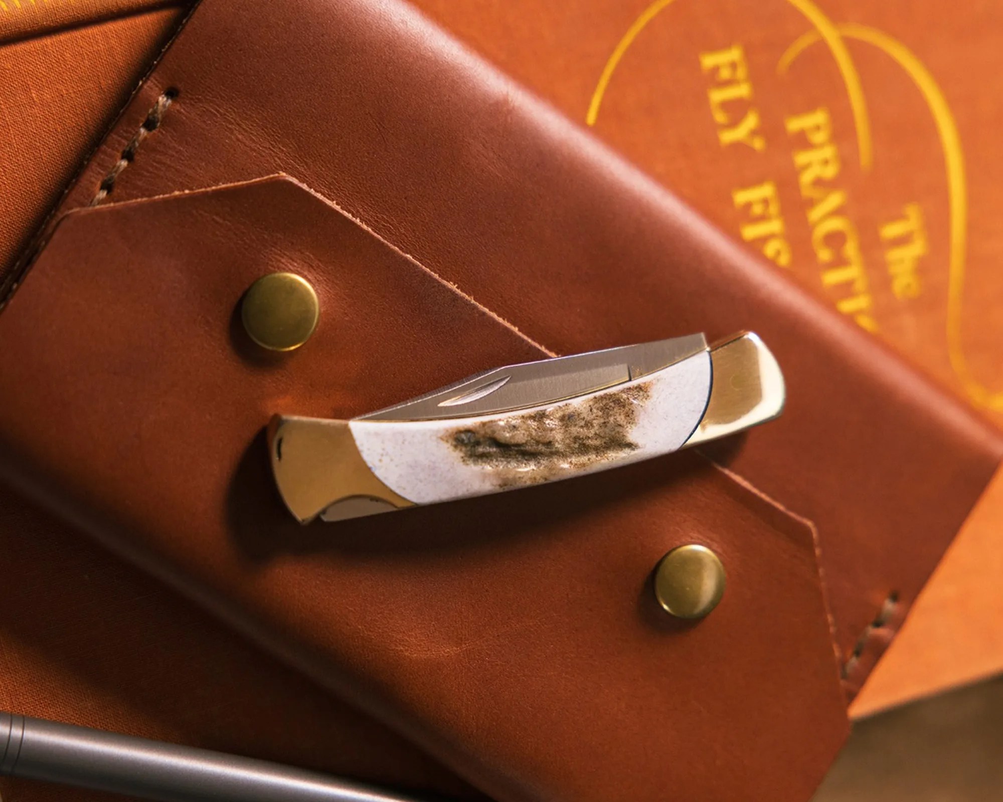 Buck The 55 Knife Custom knife on leather wallet atop fly fishing book