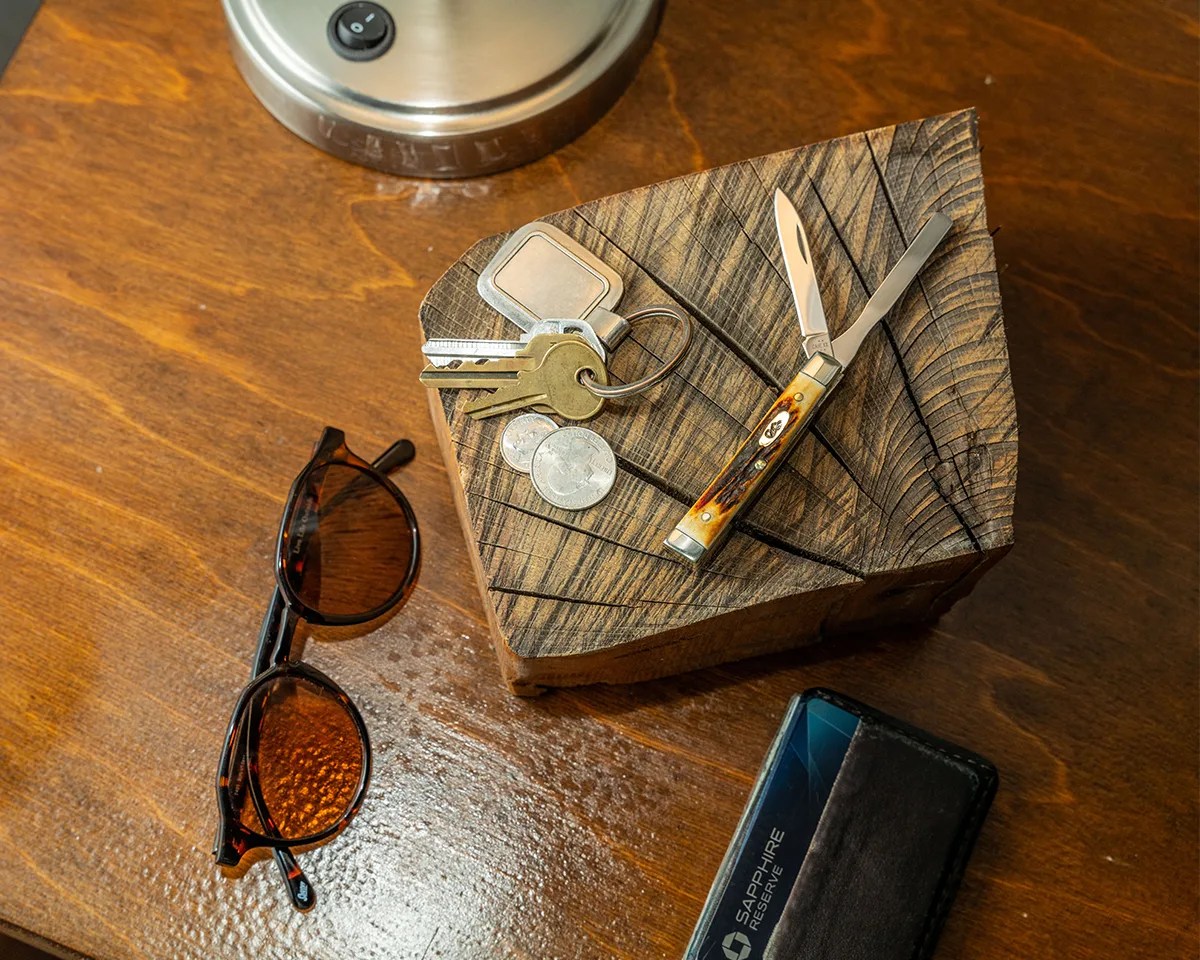 Case Baby Doc on wood block next to keys and change on desk next to wallet, sunglasses and lamp