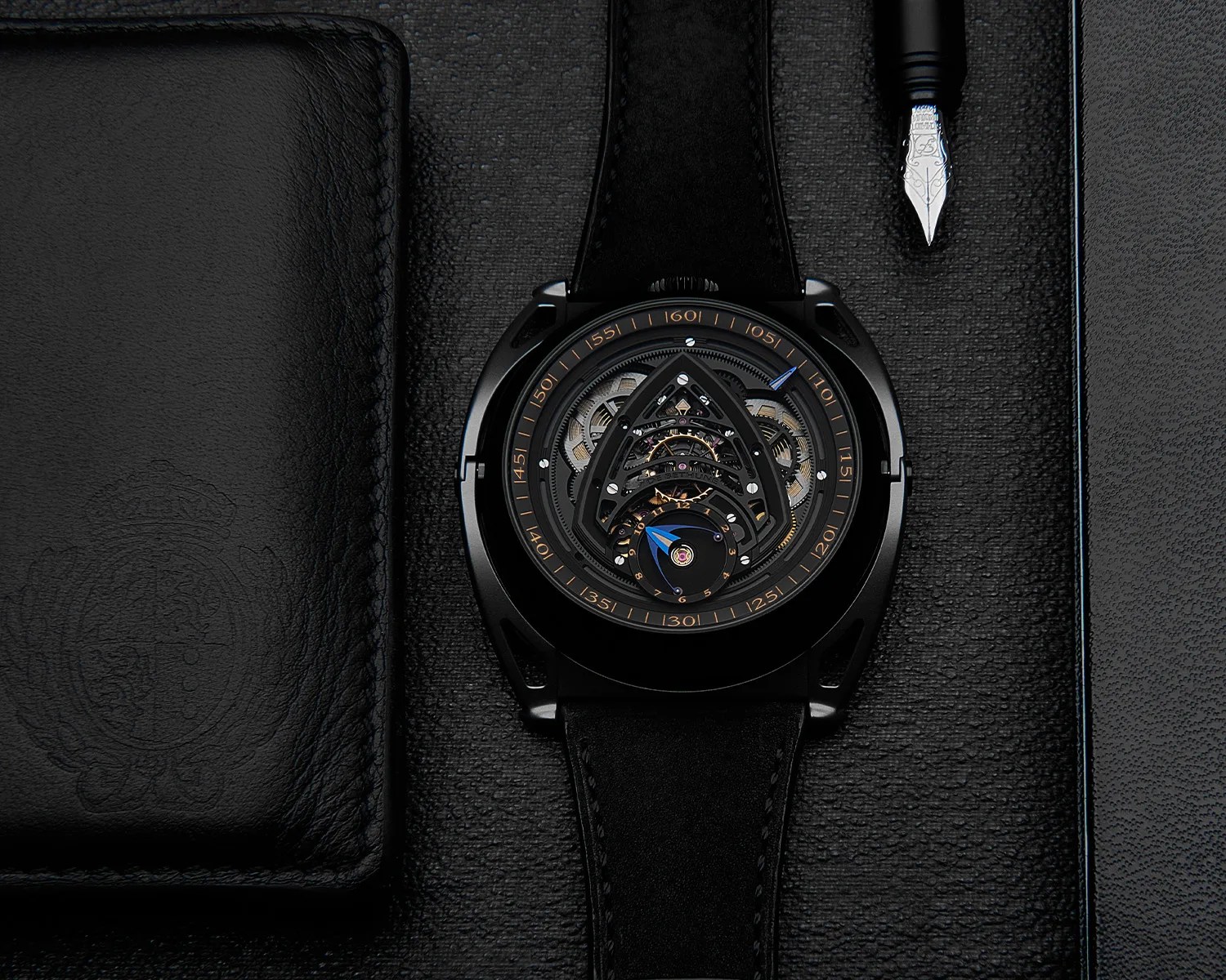 a de bethune watch on a desk next to a pen