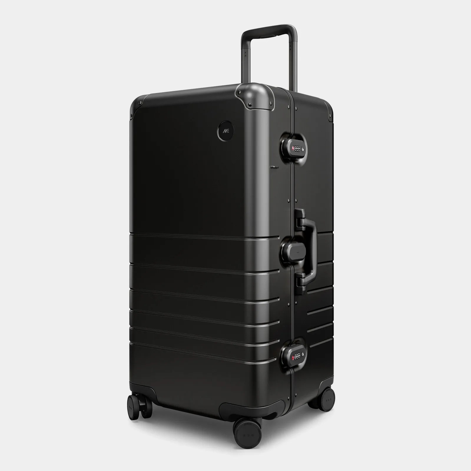 A Monos Aluminum trunk in Caviar Black shown standing at an angle with the handle slightly pulled out against a light grey background. 