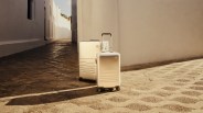 Two Mono all aluminum hard-sided suitcases shown in an empty street paved in stone. Both bags are lit by warm sunlight from the right hand side of the image casting long shadows.